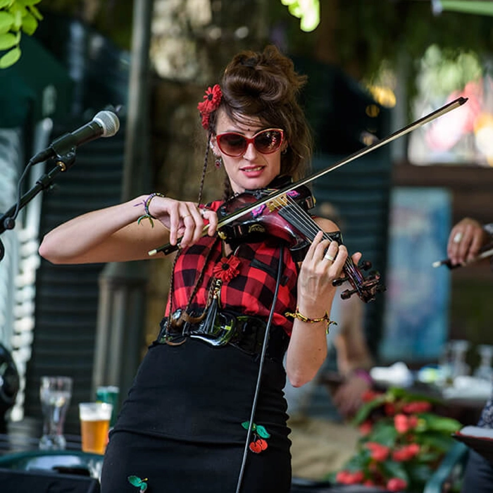 On peut voir la chanteuse du groupe El Trior jouant du violon électrique. L'artiste est légèrement penchée en arrière, arborant dans ses cheveux une fleur rouge, symbole de l'esprit guinguette.