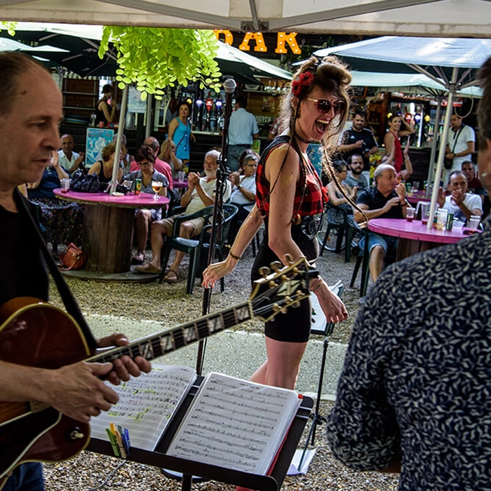 Lors de ce dernier volet du triptyque, à gauche de l'image, le guitariste du groupe est capturé en train de jouer de sa guitare. À droite, la chanteuse élève sa voix, et en arrière-plan, le public, plus en retrait dans le restaurant, est en train d'applaudir.